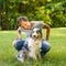 Happy young woman spending time with lovely spotted Australian Shepherd dog in green meadow on summer day