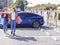 Happy  young woman standing on city parking near electric car, charging automobile battery from small city station, holding shoppi