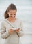 Happy young woman in sweater on beach writing sms