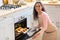 Happy Young Woman Taking Out Tray With Fresh Baked Croissants From Oven