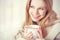 Happy young woman is under a blanket and cup of coffee on winter morning at home