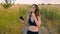 Happy young woman use smartphone and headphone standing in field at sunset, healthy lifestyle. Sportywoman runner using