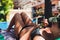 happy young woman using smartphone while relaxing on sun lounger in front of swimming pool.