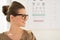 Happy young woman wearing eyeglasses in front of Snellen chart