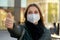Happy young woman wearing medical face mask showing thumbs up in the evening outside. Looking camera