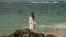 Happy young woman in a white dress raises her hands at some tropical island seashore