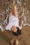Happy young woman in white shirt lying on beach in splashing waves. Top view photo. Stylish tanned girl relaxing on seashore and
