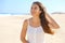 Happy young woman with white sundress on the beach. Portrait of beautiful girl with wind fluttering hair. Close up of pretty