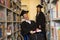 Happy young woman and woman in wheelchair in graduate gown with diploma in hands in library. Inclusive education.