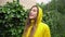 Happy young woman in yellow raincoat enjoying summer rain outdoors. Girl smiling raising arms feeling good under drizzle