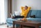 Happy young woman in a yellow sweatshirt works at home on a blue sofa with a laptop and a cat, remote work and education, staying