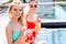 happy young women with delicious fruit beverages sitting at poolside and looking