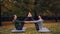Happy young women are doing pair yoga having fun and laughing sitting on mats on grass in park. Beautiful autumn nature
