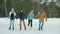 Happy youth girls and guys ice-skaing in park holding hands talking and laughing