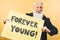 Happy youthful senior feeling forever young - Hipster mature man giving message with yellow banner