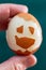 A hard-boiled chicken egg in a hand on a green background. Funny face made of eggshell on the surface. Great for breakfast