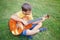 Hard of hearing preteen boy playing guitar outdoors. Child with hearing aids in ears playing music and singing song in park. Hobby