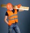 Hardy labourer concept. Man in helmet, hard hat and protective gloves holds wooden beam, grey background. Carpenter