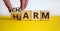 From harm to charm. Male hand turns the cube and changes word `harm` to `charm`. Beautiful yellow table, white background.