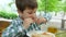 Harmful food, five year old boy eating slice of pizza sitting at a table with a glass of juice outdoors