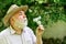 Harmony of soul. Elderly man in straw summer hat. Grandpa senior man blowing dandelion seeds in park. Mental health