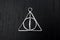 Harry Potter`s amulet of deathly hallows on black wood. Close up front view
