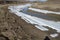 Harsh natural landscape and road along the riverbed and mountains for off-road SUV with puddles of snow and mud. Spring background