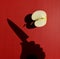 Harsh shadow of a hand holding knife above an apple cut in half