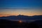 harvest moon rising behind silhouetted mountain range, with stars and clouds visible in the night sky