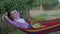 Harvest season, smiling female with basket of fruit lies in hammock and enjoys relaxing