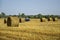 Harvested wheat field with large round bales of straw in summer. Tractor forming bales is visible background. Farmland