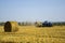 Harvested wheat field with large round bales of straw in summer. Tractor forming bales is visible background. Farmland