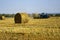 Harvested wheat field with large round bales of straw in summer. Tractor forming bales is visible background. Farmland