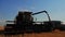 Harvester combine pours the grain into the truck on the field. Silhouette of combine harvester pours out wheat into the