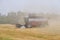 Harvester in dust clubs at work on the harvest of wheat on a huge field in the summer. Thus, the birth of bread occurs