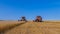 Harvesting equipment stopped in the field and combine harvesters discuss working issues. All this takes place against a clear blue