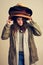 Has anybody seen my hat. Studio shot of a young woman wearing a pile of hats against a brown background.