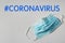 Hashtag Coronavirus and medical mask on light background, top view