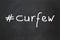 Hashtag curfew as handwritten text on chalkboard