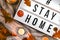 Hashtag Stay home. Text in white light box, with a background of sweater, candles, dried leaves autumn decoration. Coronavirus