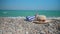 A hat, sunglasses, a sun cream and a towel is laying on a stony beach.