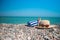 A hat, sunglasses, a sun cream and a towel is laying on a stony beach.