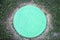 The hatch is round cast iron turquoise with a pattern of many small turquoise rings on a green grass background