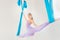 Hatha aero fly yoga concept. Beautiful young female trainer showing stretching exercises on blue hammock in white studio