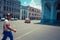 Havana / Cuba - 04.15.2015: Cuban man wearing sports cloths and a hat crossing the street as a red classic vintage car is