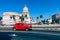 HAVANA, CUBA - DECEMBER 10, 2019: Brightly colored classic American cars serving as taxis pass on the main street in front of the