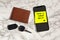 Have a great day romantic and sweet handwritten note on yellow posit stick to mobile phone next to car key and leather wallet in