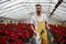 Having a distant look. Portrait of beautiful young guy in the hothouse taking care of flowers