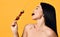 Having fun laughing brunette woman with bare shoulders holds a wooden skewer with berries and eats bites cherry isolated on yellow