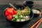 Hawaiian salmon poke bowl with seaweed, cucumber, avocado and sesame seeds on black wooden table.